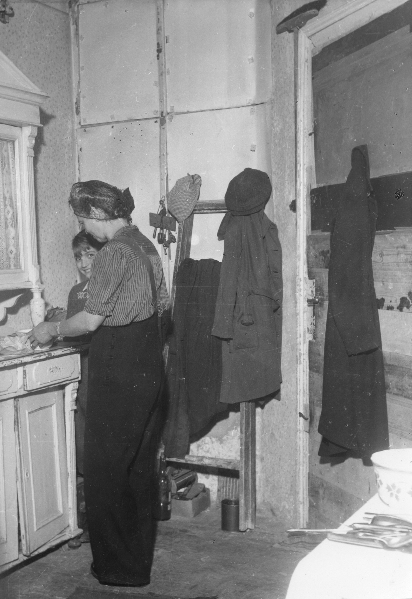 "Die Küche in Wien. Sie schliesst mit einer primitiven Brettertür. Auch hier sind die fehlenden Glasscheiben des Küchenfensters durch Kartonstücke ersetzt. Das Buffet ging bei einem Bombardement aus den Fugen." Frau beim Kochen mit Kind, Wien 19