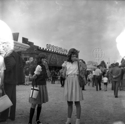 Jahrmarkt, zwei junge Frauen mit Zuckerwatte, dahinter eine Geisterbahn, um 1960