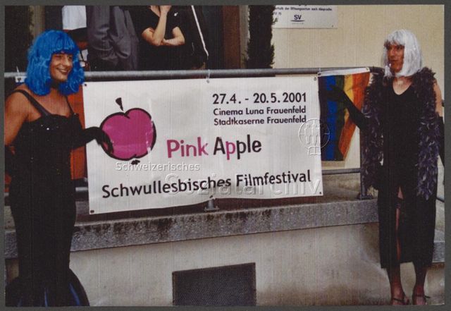 Frauenfeld Demo Pink Apple 2001 (27.04–20.05.2001, Frauenfeld) – zwei Drag Queens vor einem Werbebanner des schwullesbischen Filmfestival "Pink Apple"