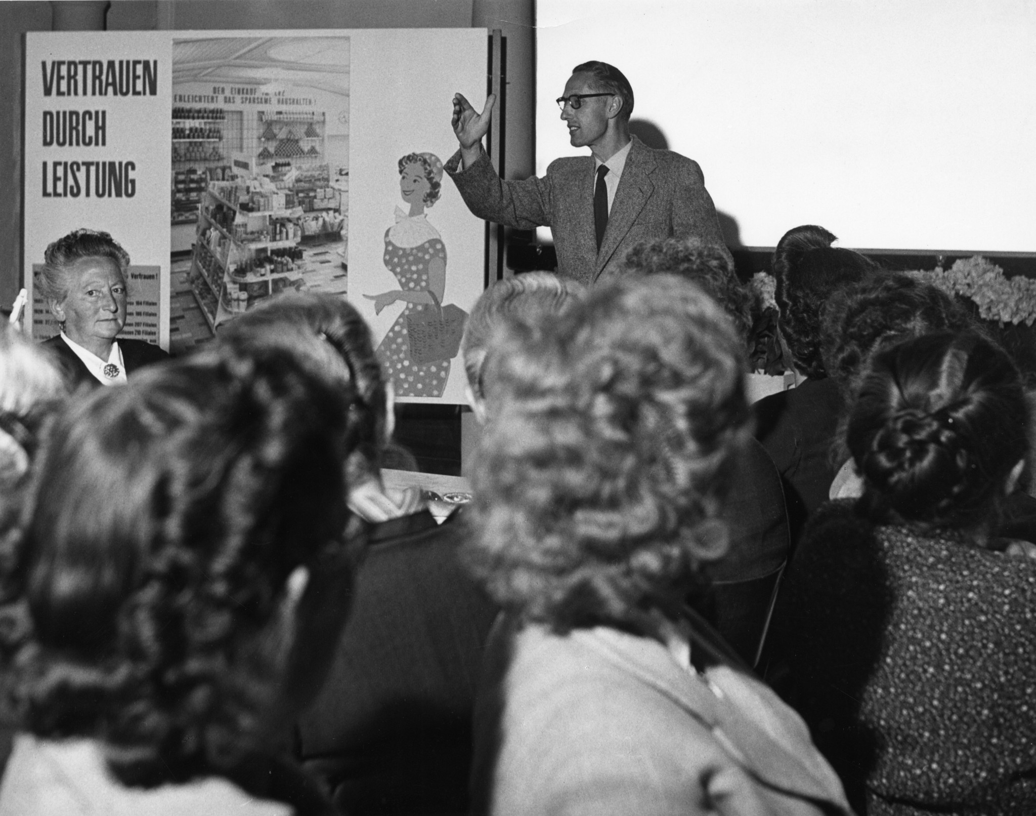 Mitarbeiterversammlung 1940er / 50er Jahre - Vortrag eines Mannes mit Plakat "Vertrauen durch Leistung", Frauen am Zuhören