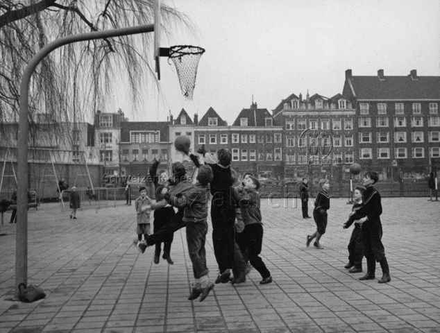 "Ein Spielplatz in der Stadtmitte (Amsterdam)" - Kinder spielen Basketball, im Hintergrund wird geschaukelt; um 1960