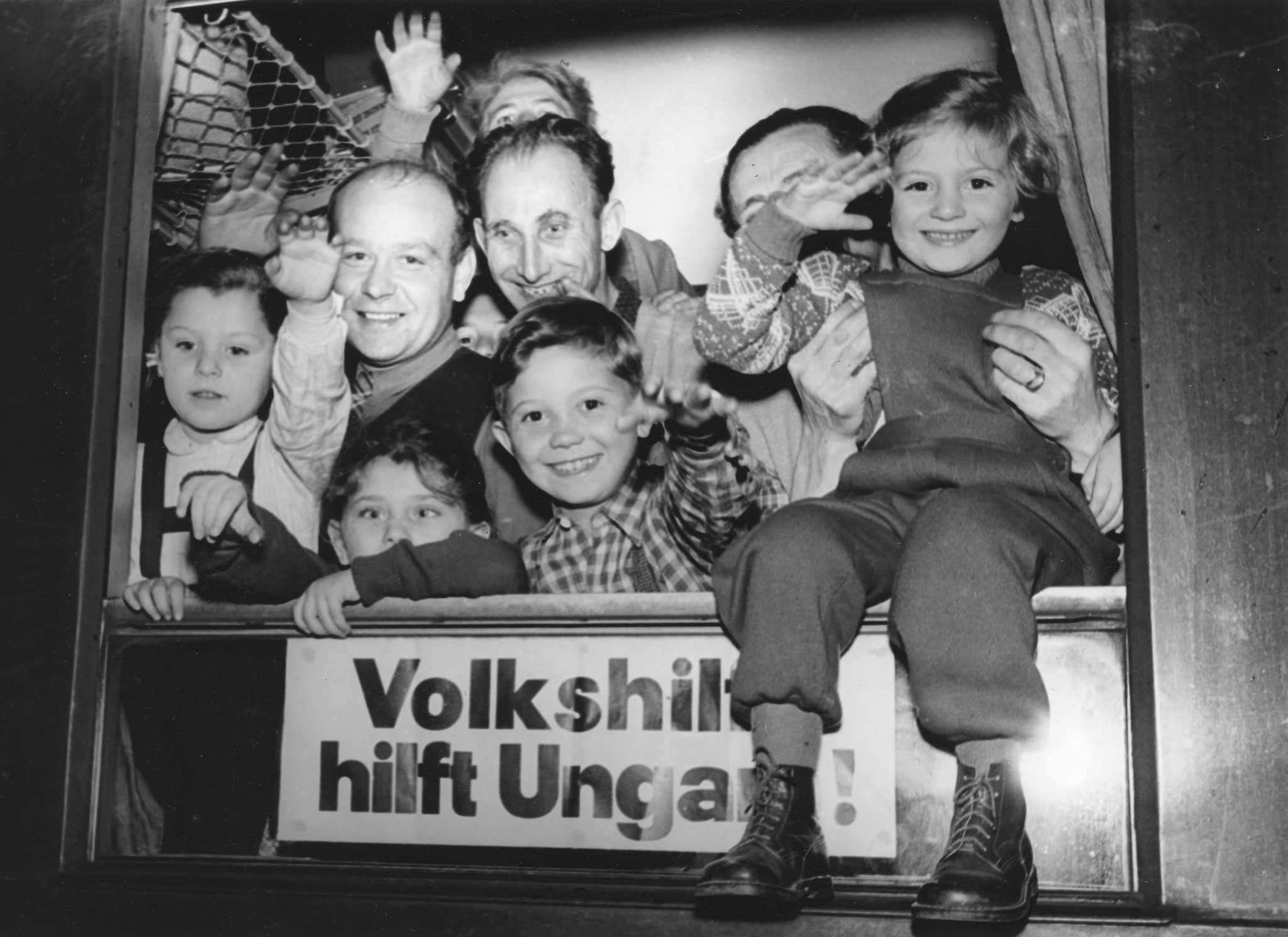 Männer und Kinder schauen aus einem Puppentheater mit der Aufschrift "Volkshilfe hilft Ungarn" und lächeln