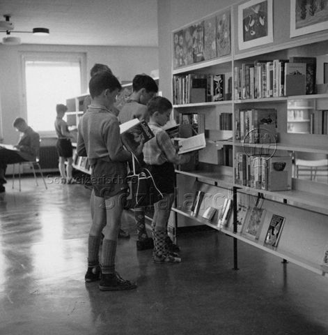 "Bibliothekfiliale Altstetten" - Kinder beim Lesen vor dem Bücherregal; um 1965