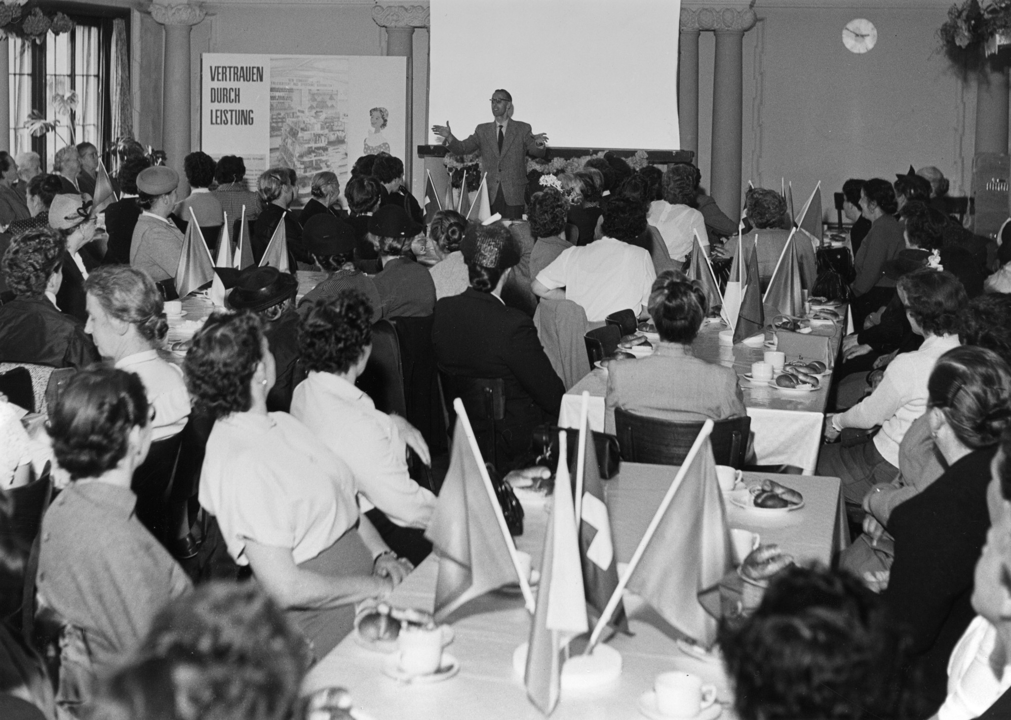 Mitarbeiterversammlung 1940er / 50er Jahre - Vortrag eines Mannes mit Plakat "Vertrauen durch Leistung", Frauen am Zuhören