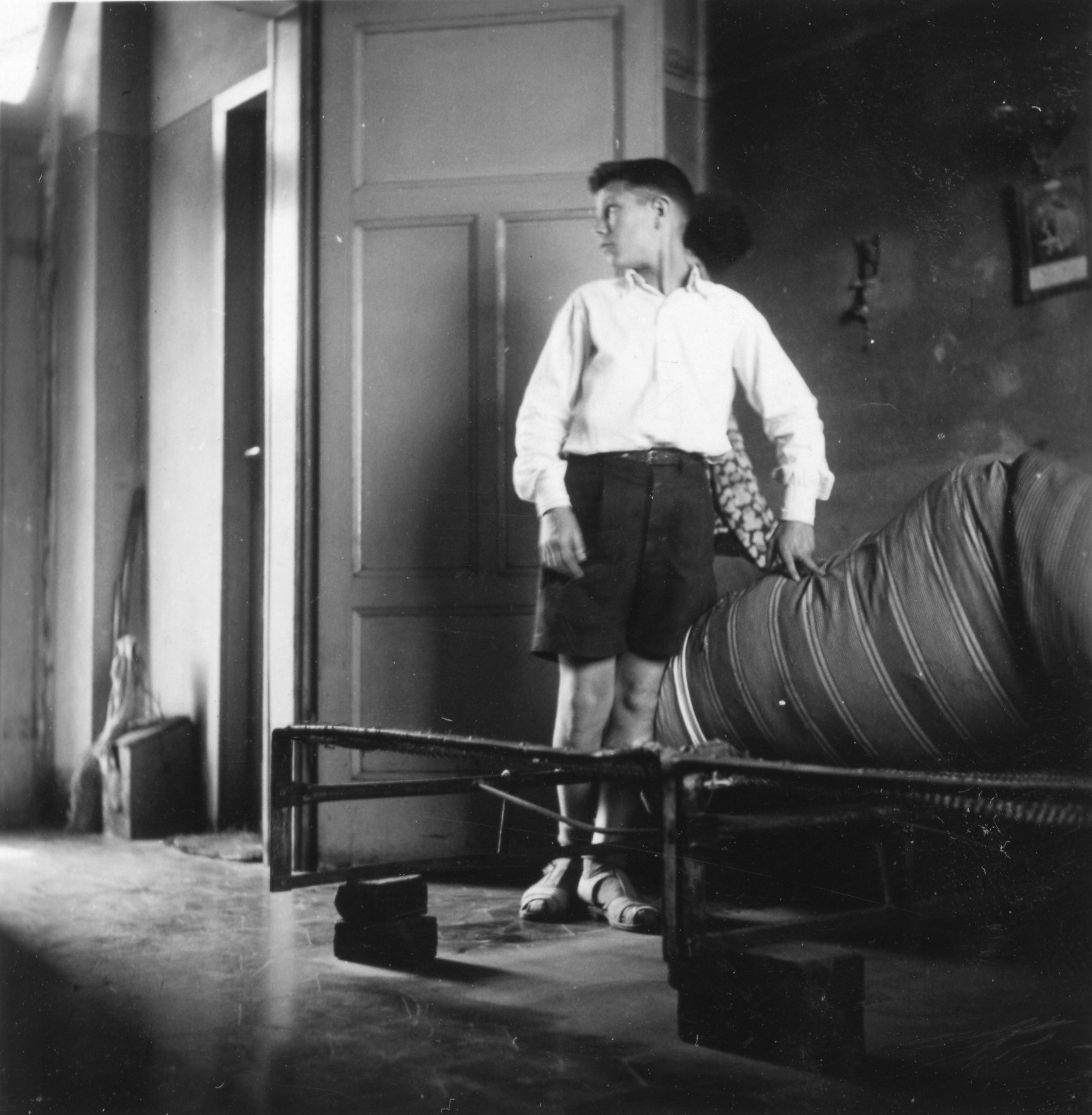 "Milano, Sommer 1946. Intérieurs bei Hausbesuchen für die AERMO-Möbelverteilung."; ein Knabe demonstriert die ärmlichen Wohnverhältnisse anhand der Pritsche