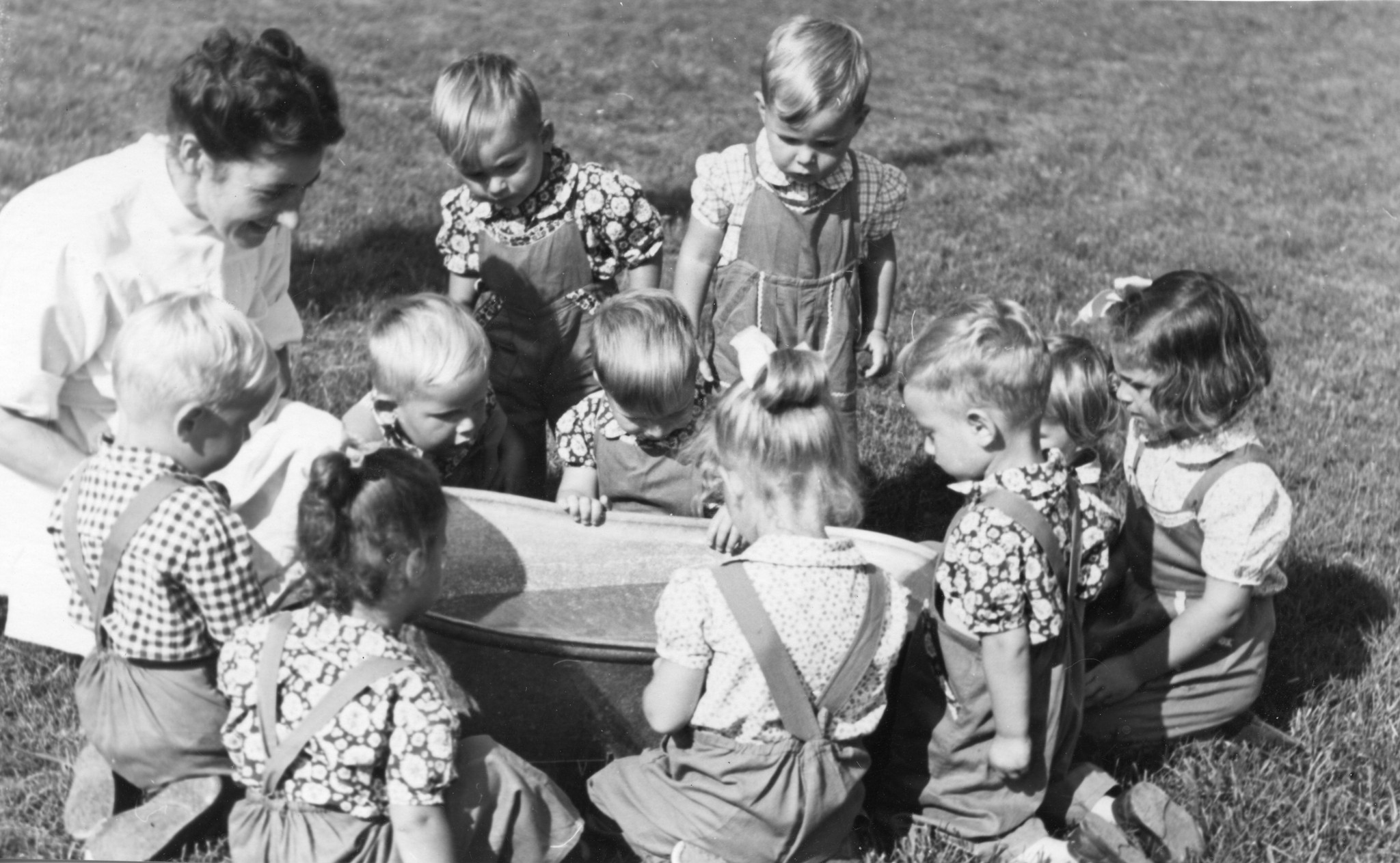 "Säuglingsheim Innsbruck - Schweizer Spende u. SAH"; Kinder und eine Betreuerin sitzen um eine Wanne und bestaunen das Wasser