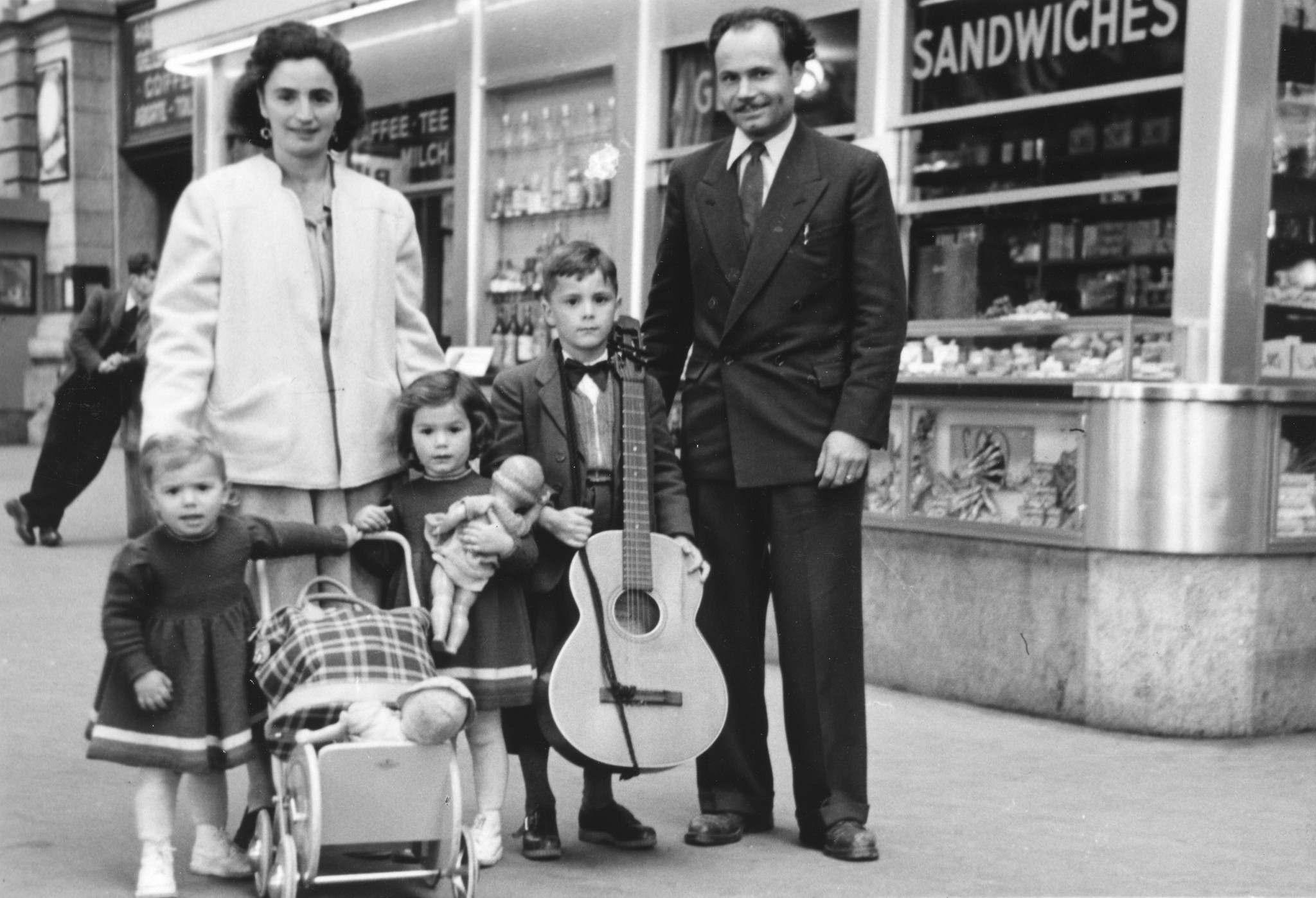 "Australien - Transport Flüchtlinge aus allen Ländern [Flüchtlings-Auswanderung nach Australien, Zwischenverpflegung in CH]  - 25. Oktober 1949", Flüchtlingsakt. IRO, Flüchtlingsfamilie mit Puppenwagen und Musikinstrument im Bahnhof (?)