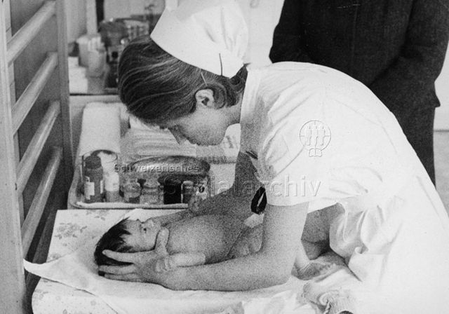 "Mütterberatung Schiers" - Krankenschwester kümmert sich um Säugling; um 1970