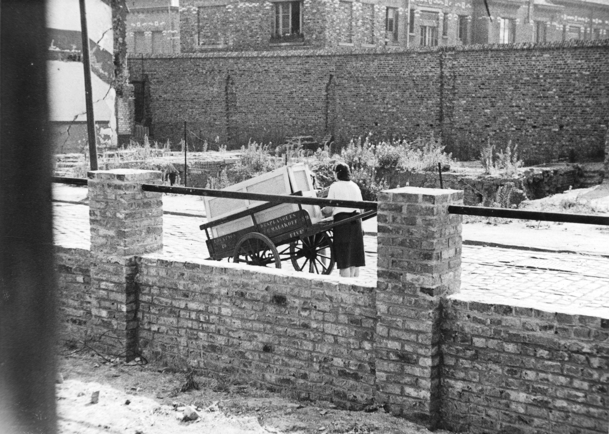 "Fives [Stadtviertel von Lille, Nord-Pas-de-Calais] Bénéficiaire de mobilier AERMO", eine Frau schleppt einen Möbelstück, aus der Möbelverteilung vom SAH-Sozialzentrum, um 1946