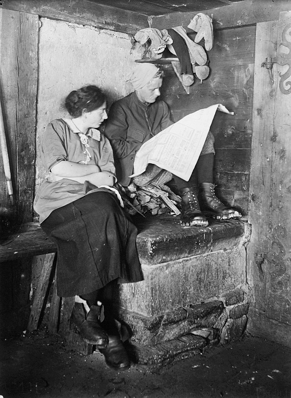 Zwei Frauen der Wandervogel-Ortsgruppe Bern in der Selital (Ski-)Hütte lesen eine Zeitung - Eine Frau auf einem Holzstapel sitzend (