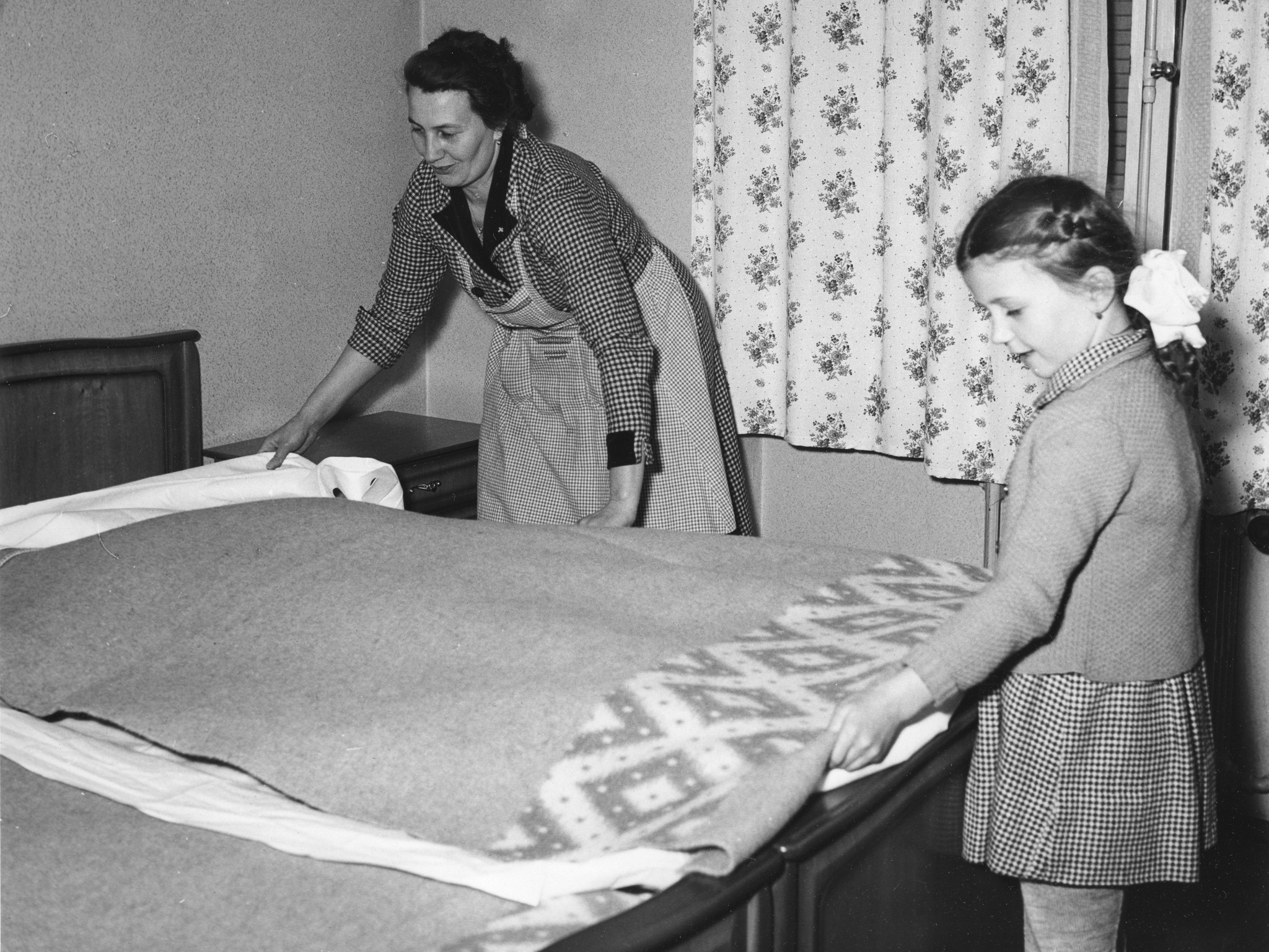 Eine Frau und ein Mädchen breiten eine Wolldecke über ein Bett