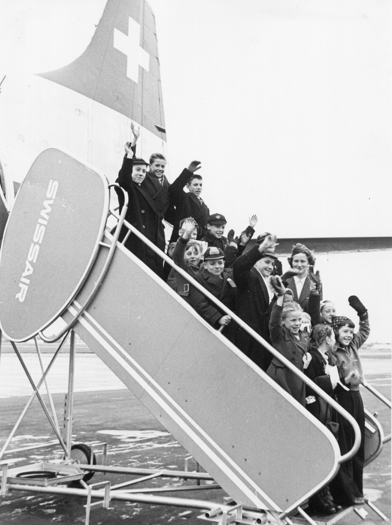 Kinder stehen auf dem Einstieg zum Flugzeug und winken