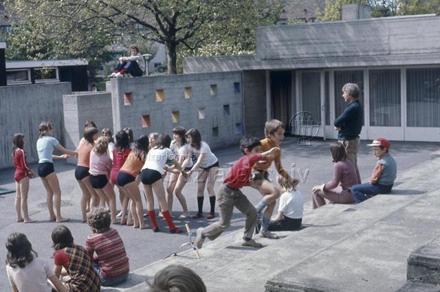 "Kinderzirkus/ Kindertheater: Zirkus-Probe FZA Buchegg, Zürich" - Mädchengruppe in Unterhosen übt eine artistische Figur, andere Kinder und ein Erwachsener schauen ihnen dabei zu; um 1970