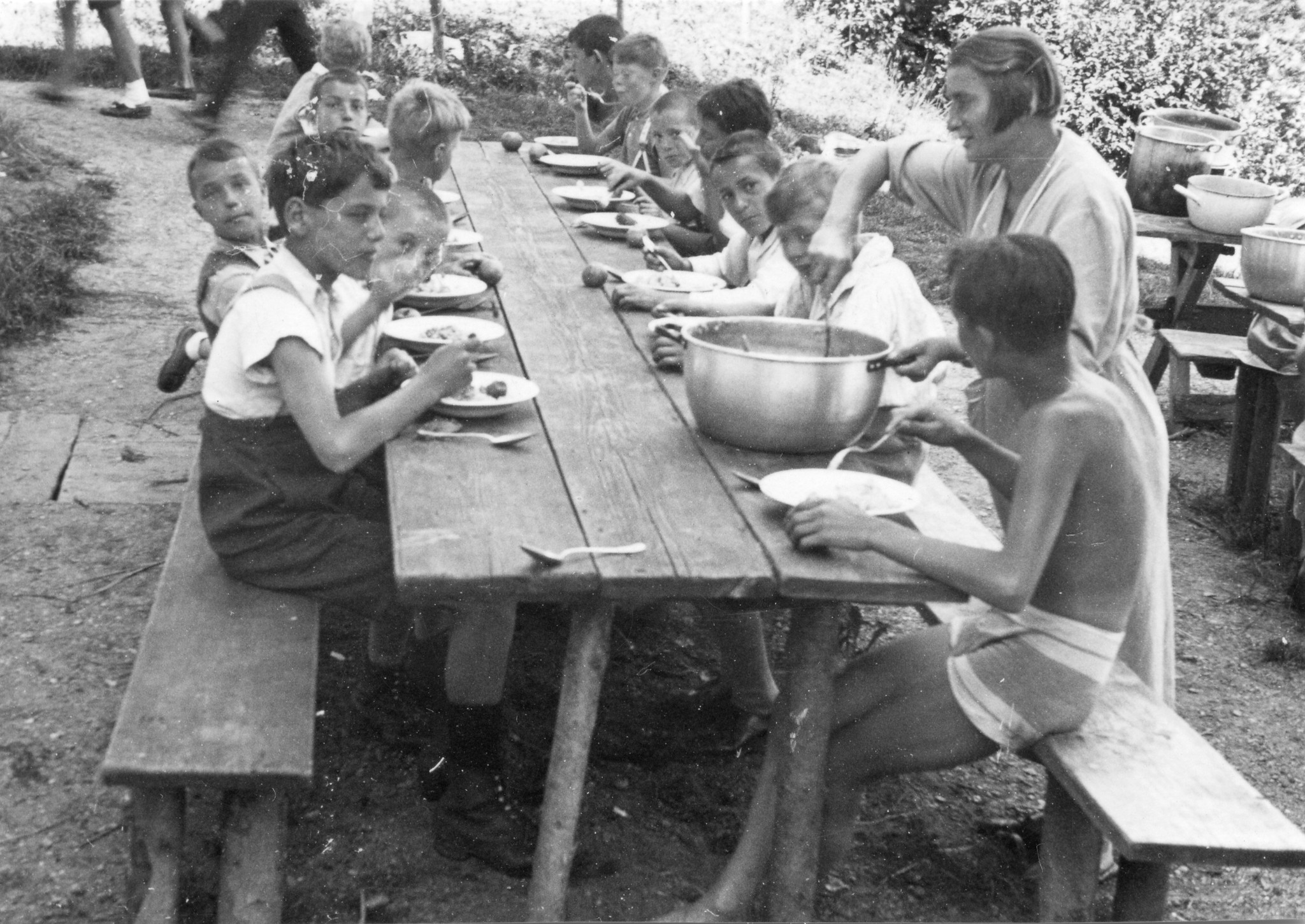 Kinder und Betreuerin sitzen draussen und essen