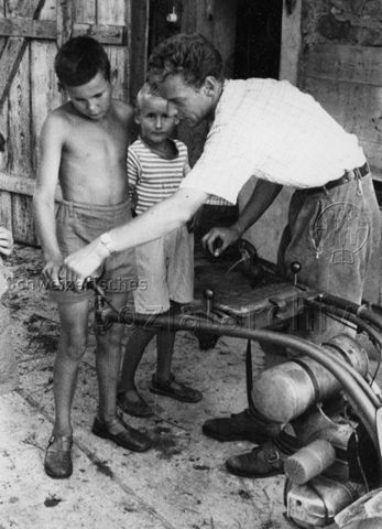 PraktikantInnenhilfe - Praktikant lehrt Jungen den Umgang mit der Mähmaschine; um 1965