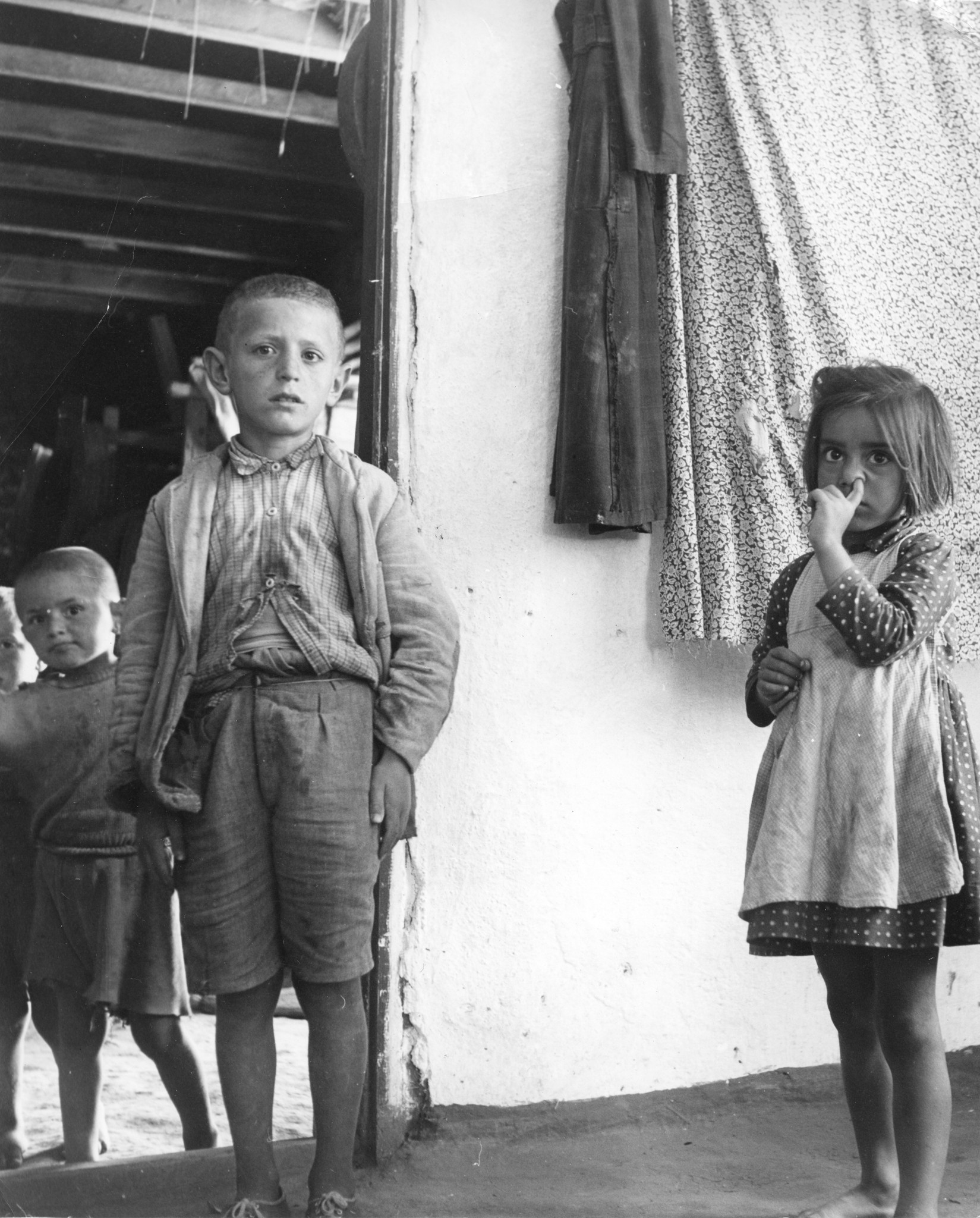 Kleine Kinder stehen in einem Eingang; ein Mädchen bohrt in der Nase