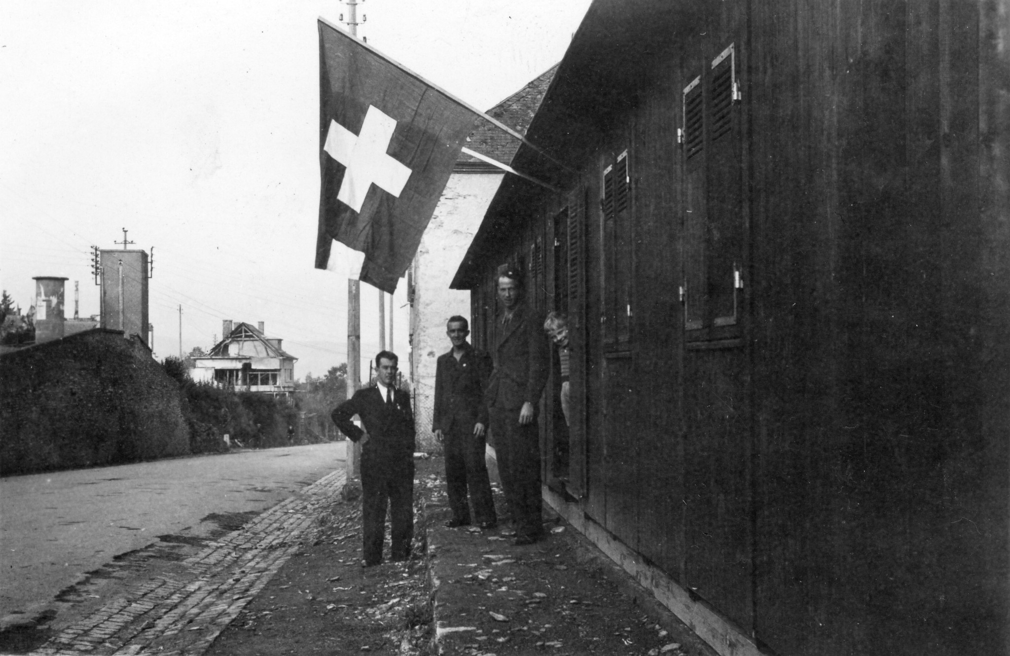 "Unsere Mannschaft bei der Arbeit und bei Erholung"; Männer stehen vor einem Haus mit Schweizer Flagge
