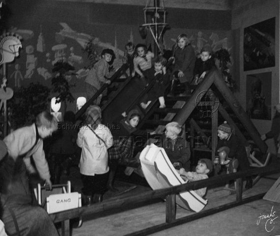 Spielhaus - spielende Kinder auf und um ein Spielhaus, eine Seite des Daches dient als Rutschbahn; um 1955