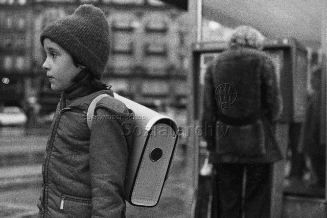 "Kind + Grossstadt" - Mädchen mit Schultheke steht an der Bushaltestelle