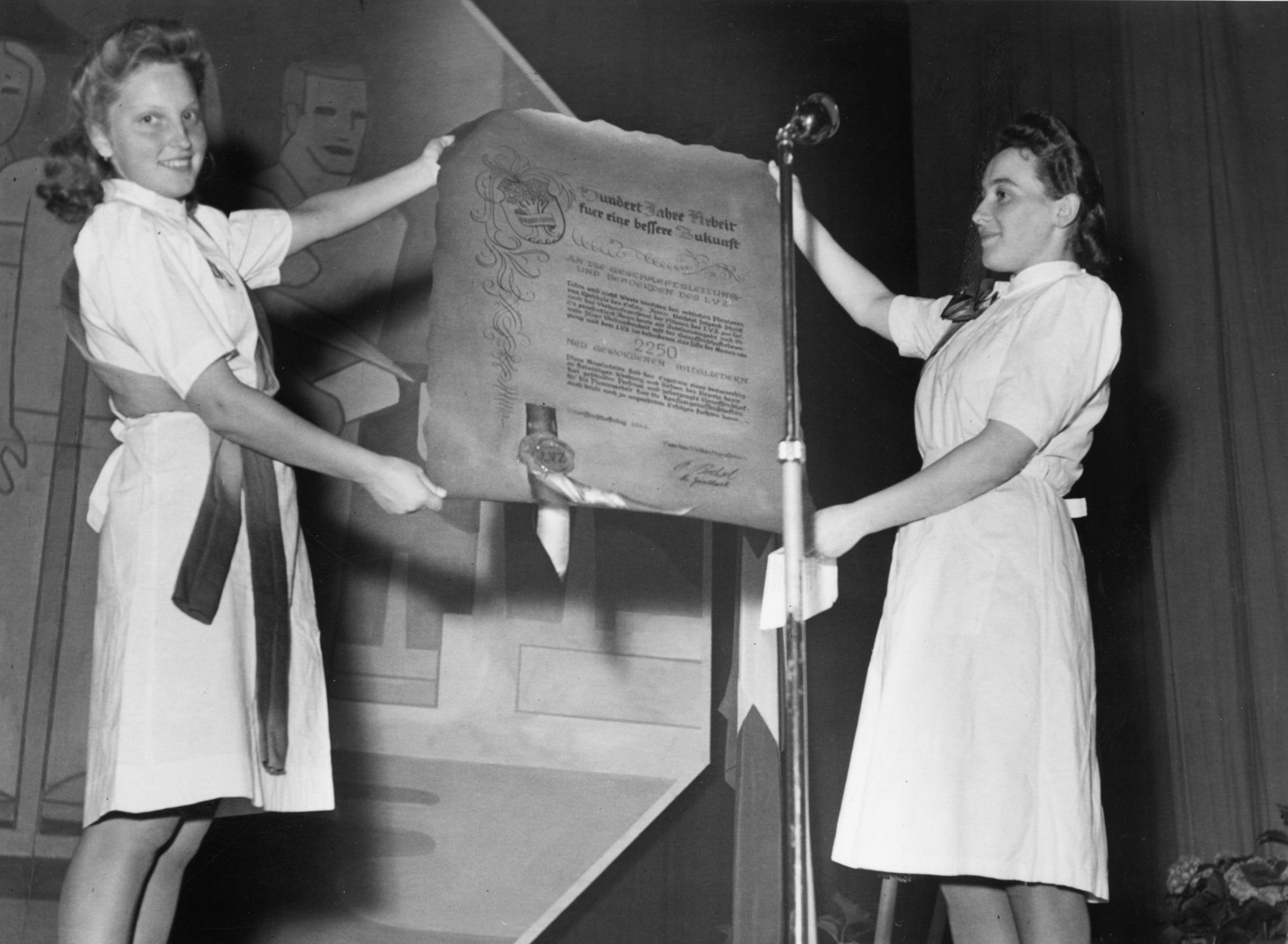 Jubiläum 100 Jahre Genossenschaftsbewegung in der Tonhalle Zürich, 1944 (anlässlich der Gründung der ersten modernen Genossenschaft 1844 in Rochdale, Nordengland): Frauen präsentieren Urkunde