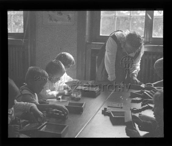 Diaserie zum Thema Kindergarten / Schulkind; Kinder an Tisch sitzend bilden mit Holzwürfeln Muster nach; Betreuerin am Tischende stehend; um 1930