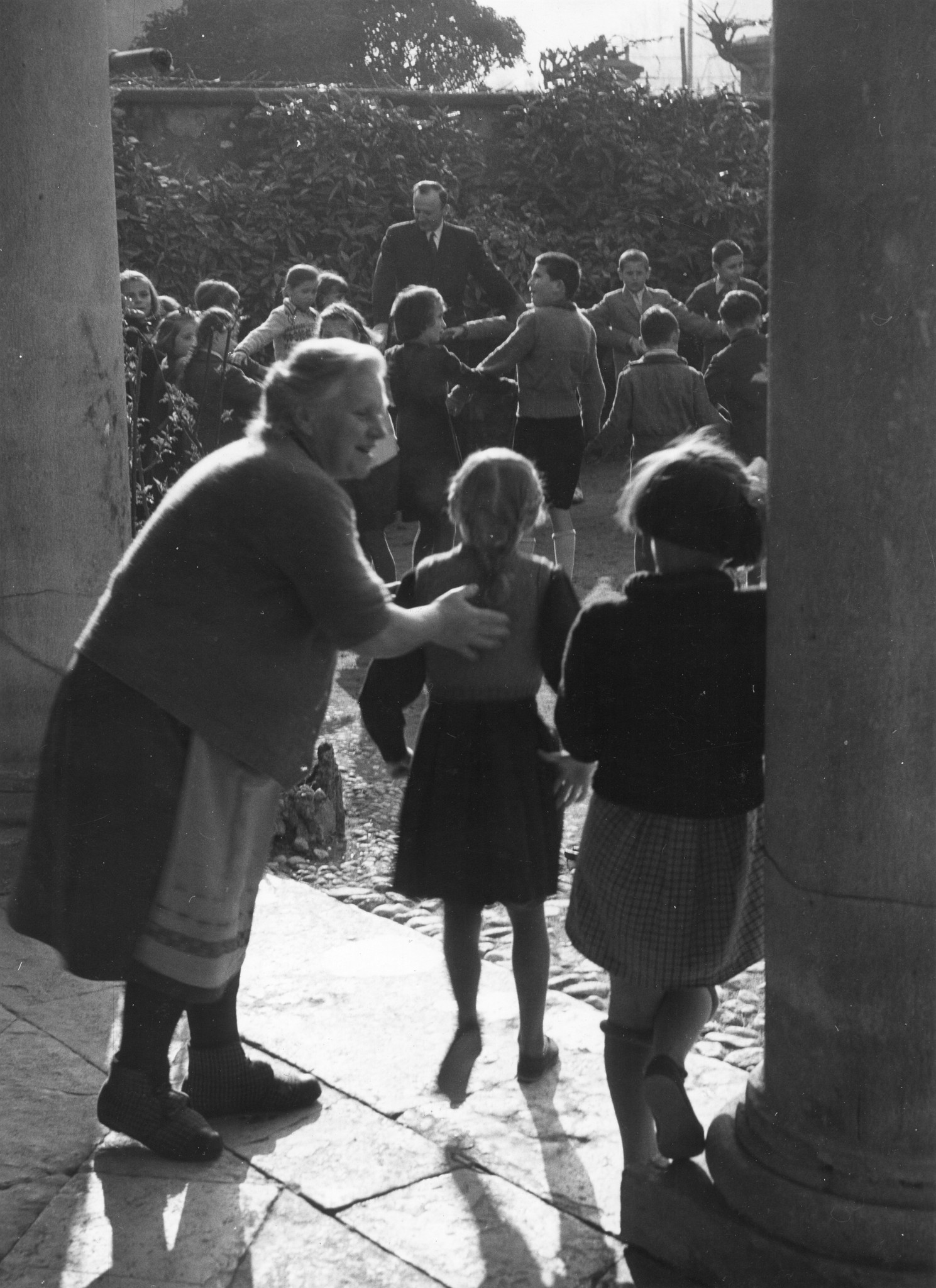 Betreuer tanzen mit den Kindern einen traditionellen jugoslawischen Tanz; eine weitere Betreuerin animiert zwei Mädchen auch mitzumachen