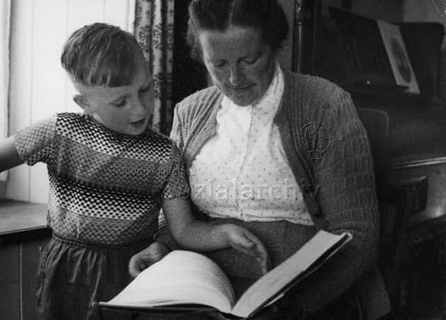 Frau und kleiner Junge sehen sich ein Buch an; um 1950