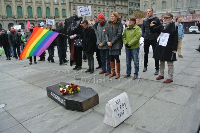 Kundgebung in Bern gegen die Familieninitiative der CVP (16.11.2013, Bern) – Sarg: Gleichstellung, davor: "RIP - Art. 8 BV - 1848–?"; Alicia Parel (4. Person v. rechts), verschleierte Person mit Regenbogenflagge, "Depuis 30 ans je paie les mêmes impots que les héteros ! Aujourd'hui, je veux les même droits ! Un point c'est tout !" (rechts), "NEIN !!! Zur Diskriminierung in der Verfassung / NON !!! Aux discriminations dans la Constitution" (mitte)