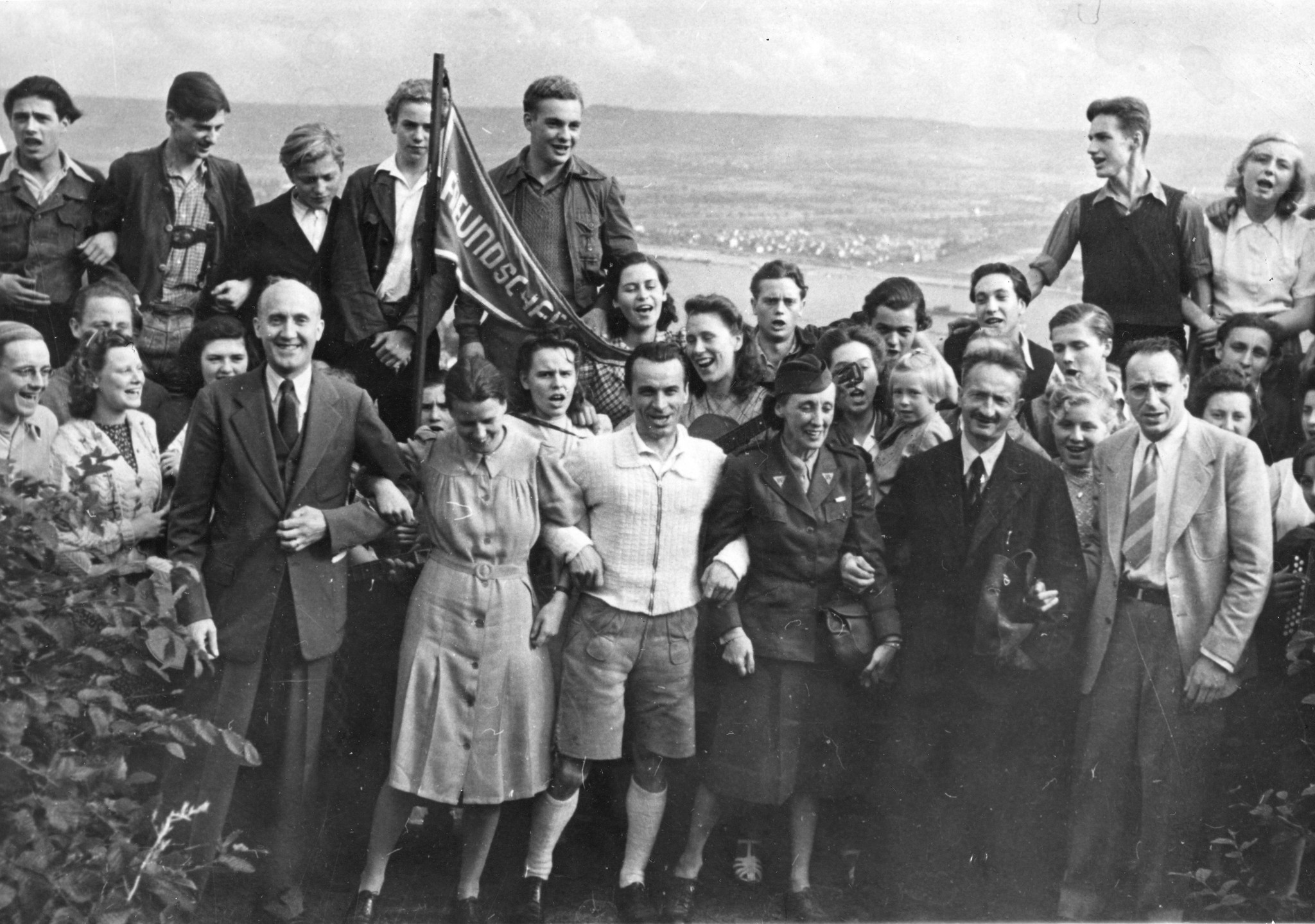 Gruppenfoto beim Gesang der Roten Falken mit den Besuchern aus Amerika, in der Mitte die Fahne der Freundschaft