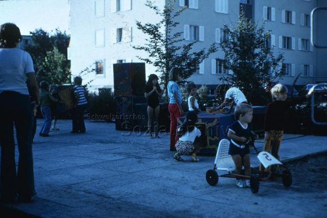 "Zeichnen und Malen: Spielaktion Volketswil ZH" - Kinder bemalen grosse Holzkisten auf einem Spielplatz mit Plattenboden; um 1970