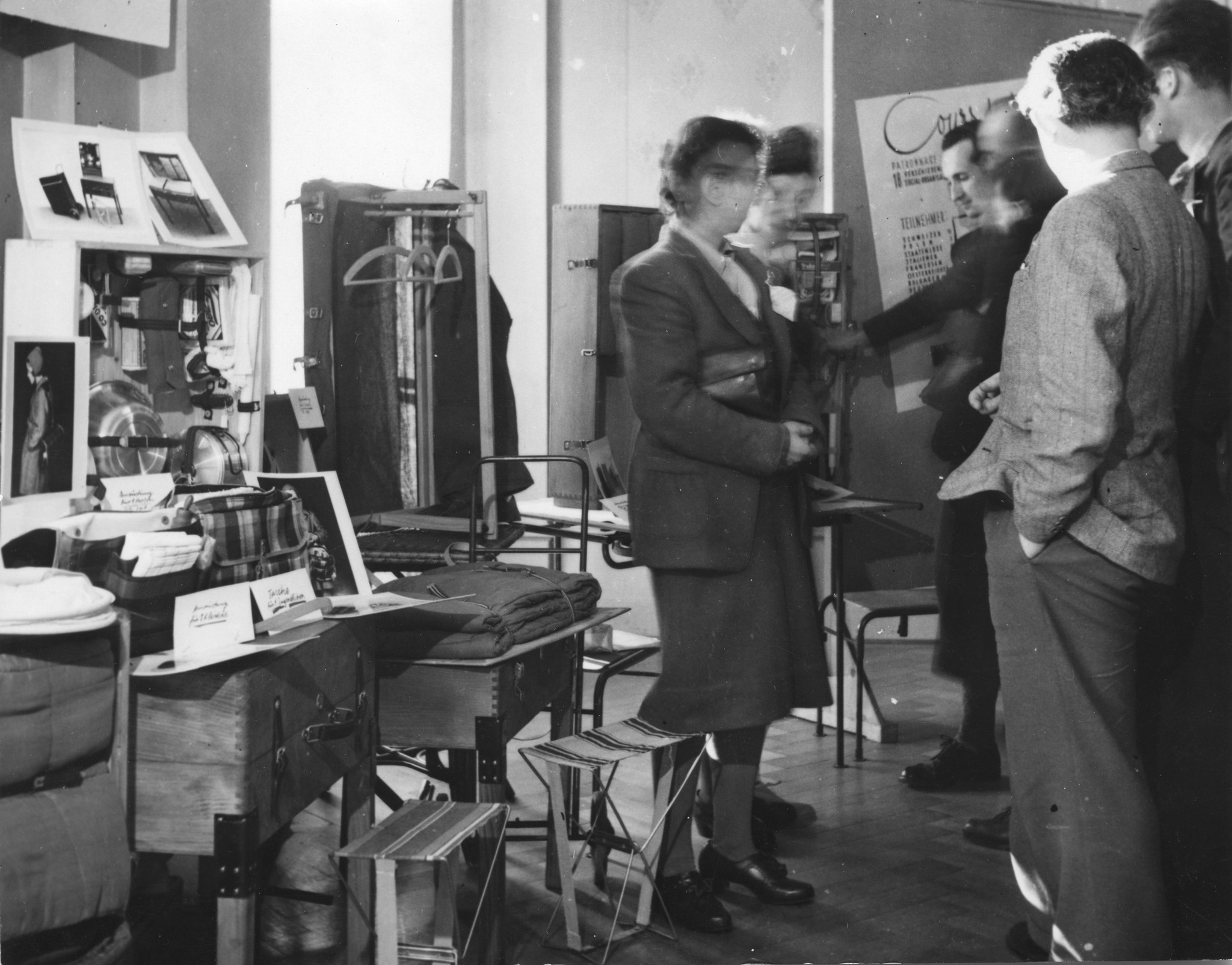 "Flüchtlingskongress, Montreux, Februar 1945. Ausstellung des SAH von Flüchtlings-Ausstattungsmaterial. Erfinder: Knellesen", Gäste besuchen eine Ausstellung mit Hilfsgütern (Küchenausstattung, Decken, Kleidungskoffer, Hocker...)