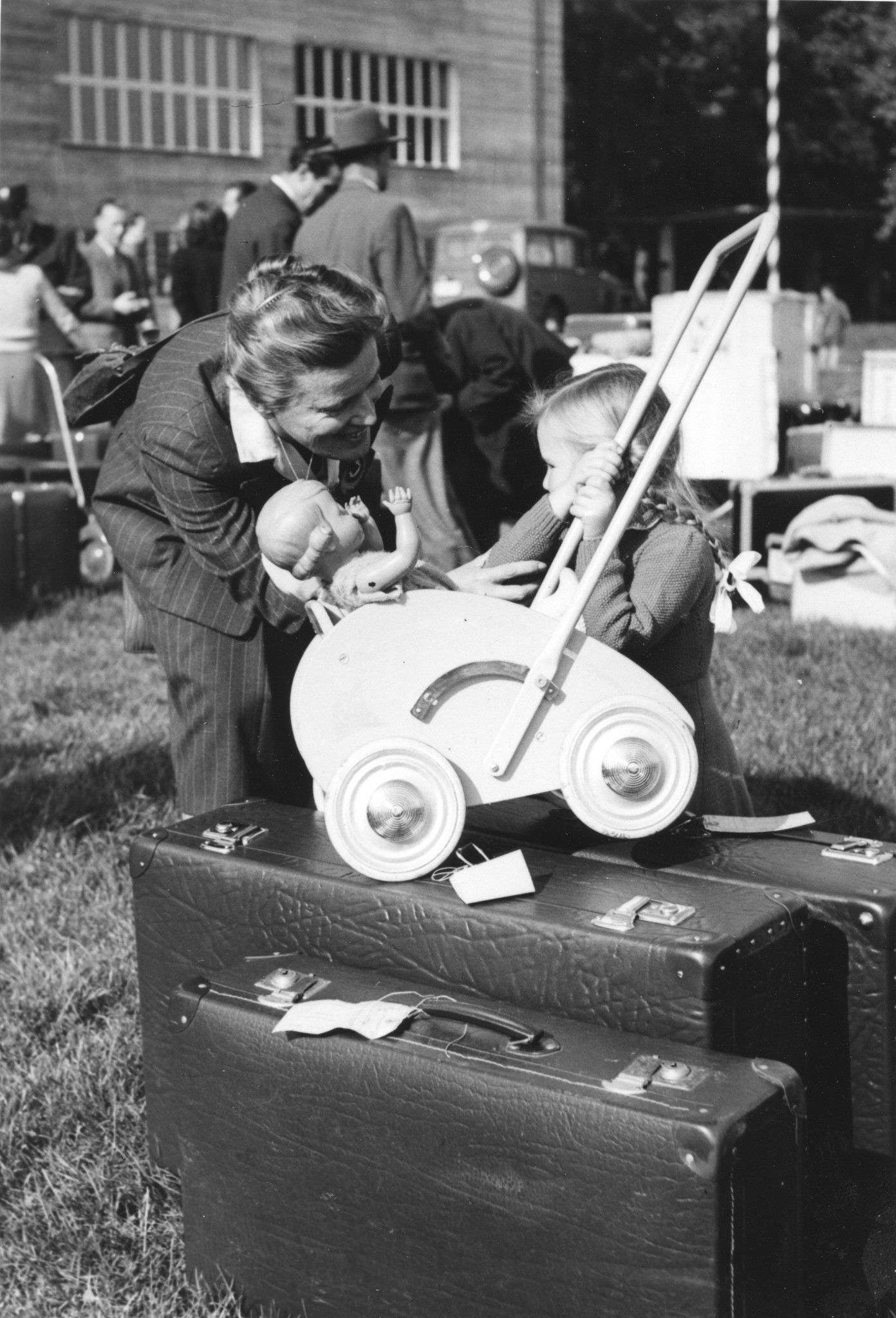 "Australien - Transport Flüchtlinge aus allen Ländern [Flüchtlings-Auswanderung nach Australien, Zwischenverpflegung in CH]  - 25. Oktober 1949", Flüchtlingsakt. IRO, Flüchtlingsmädchen mit Puppenwagen und Gepäck im Gespräch mit einer Frau