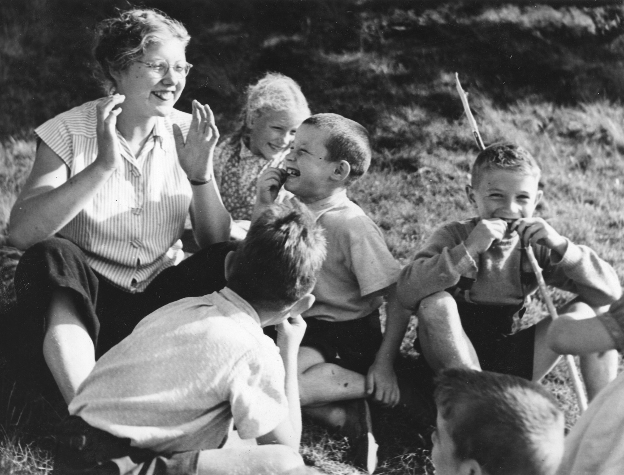 Ferienkolonie Landmark: Kinder und Betreuerin sitzen lachend auf einer Wiese