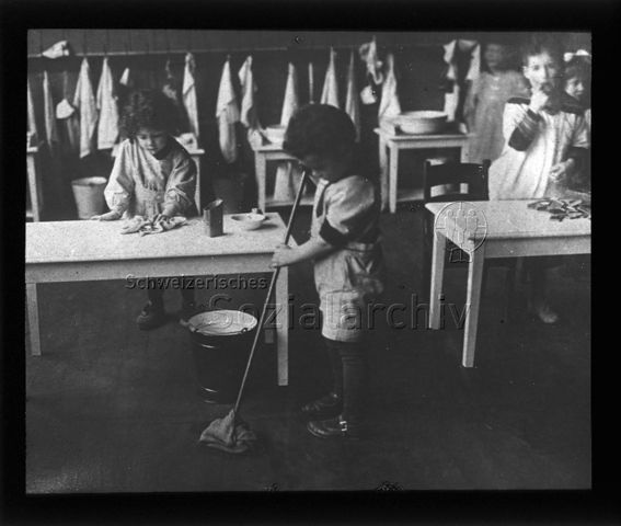 Diaserie zum Thema Kindergarten / Schulkind; Kinder beim Putzen vom Boden und von Tischen;  im Hintergrund verschiedene Tücher und Lappen und Waschschüsseln; um 1930