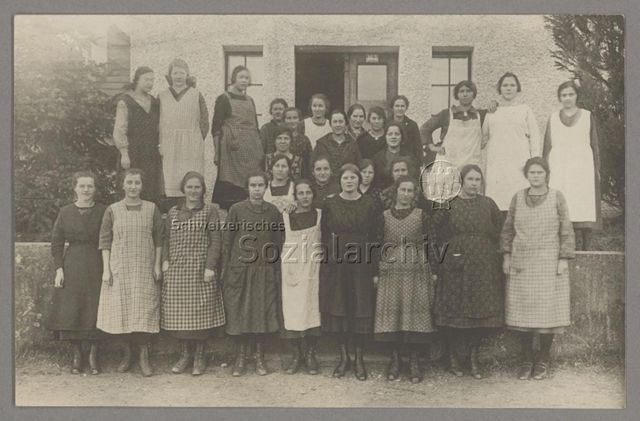 Gruppenporträt junger Frauen mit Schürzen vor Häuserfassade, um 1920
