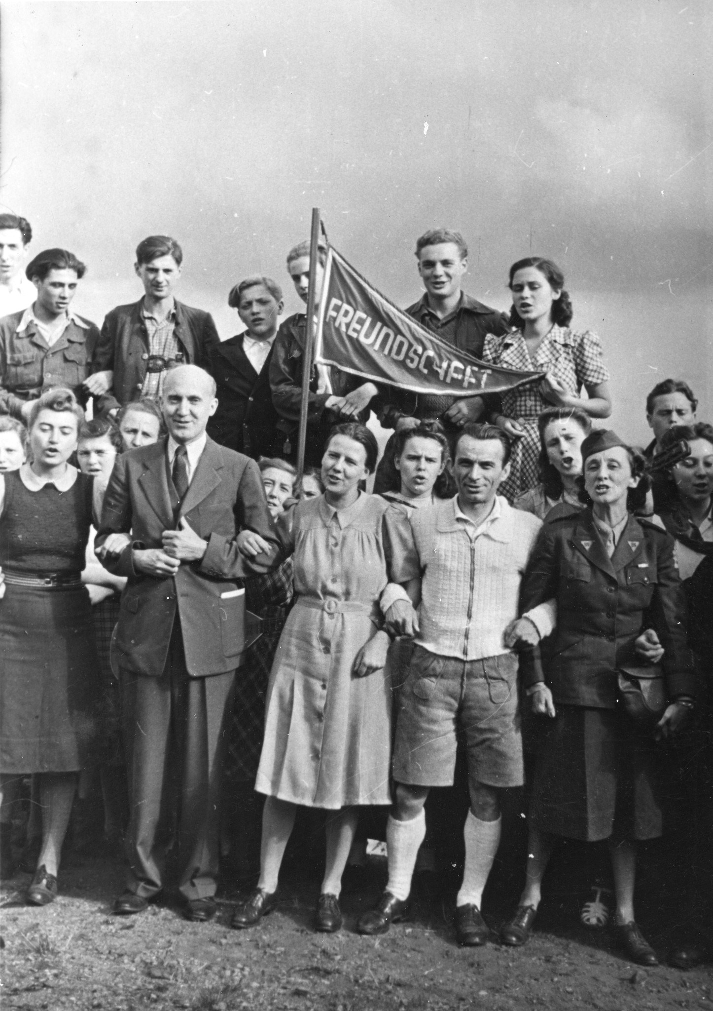 Gruppenfoto beim Gesang der Roten Falken mit den Besuchern aus Amerika, in der Mitte die Fahne der Freundschaft