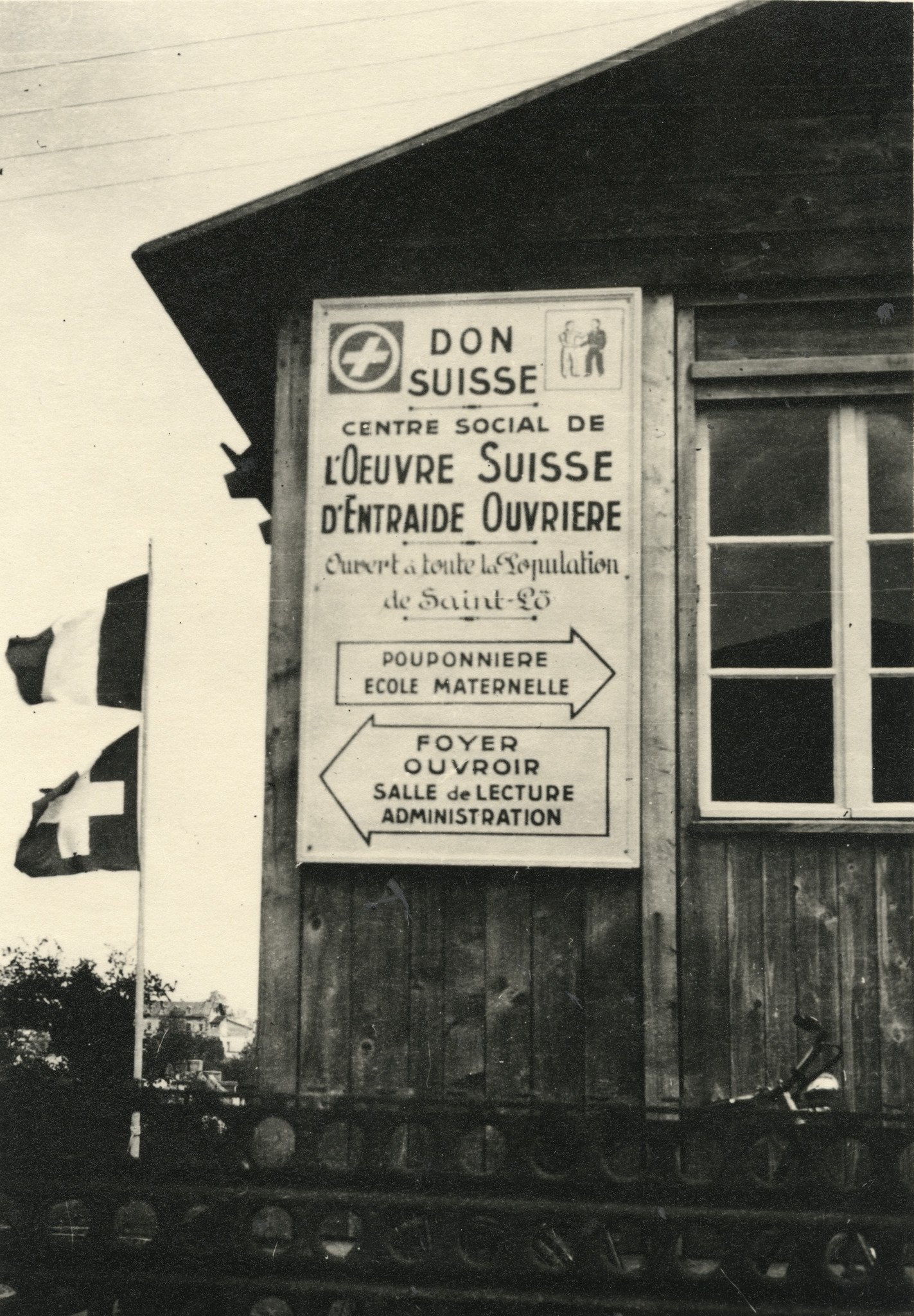 "Saint-Lô, Inauguration, 4 Mai 1947",Wandtafel: "Don Suisse, Centre sociale de l'Oeuvre Suisse d'Entraide Ouvrière, Ouvert à toute la population de Saint-Lô,Pouponnière, Ecole Maternelle, Foyer, Ouvroir, Salle de Lecture, Administration", Fahnen