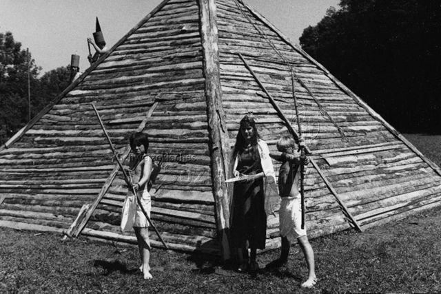 "Ferienpass" - Kinder spielen Indianer und stehen vor einer Holzpyramide; 1980