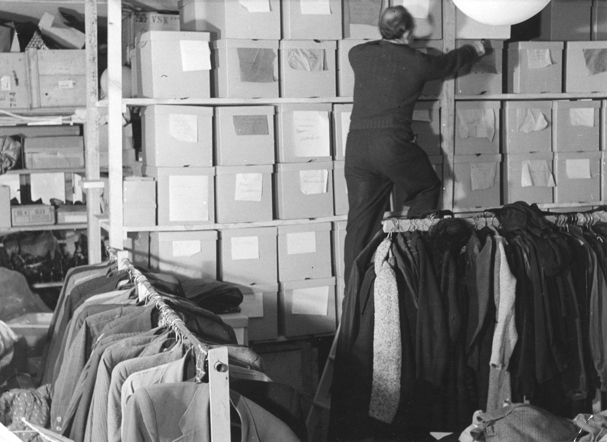 "Aus unseren Sammellager in dem Kernstrasse-Schulhaus, 1946", Mann bei der Arbeit im Hilfsgüterlager des SAH (Jacken, Kleidungen, Kisten)