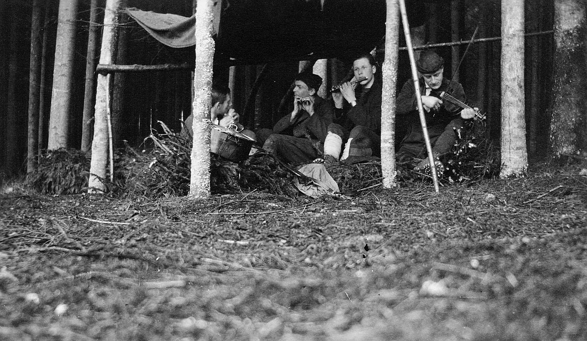Drei Wandervögel spielen Querflöte und ein Wandervogel spielt Geige in einer mit einem Tuch gebauten Hütte im Wald (um 1921)