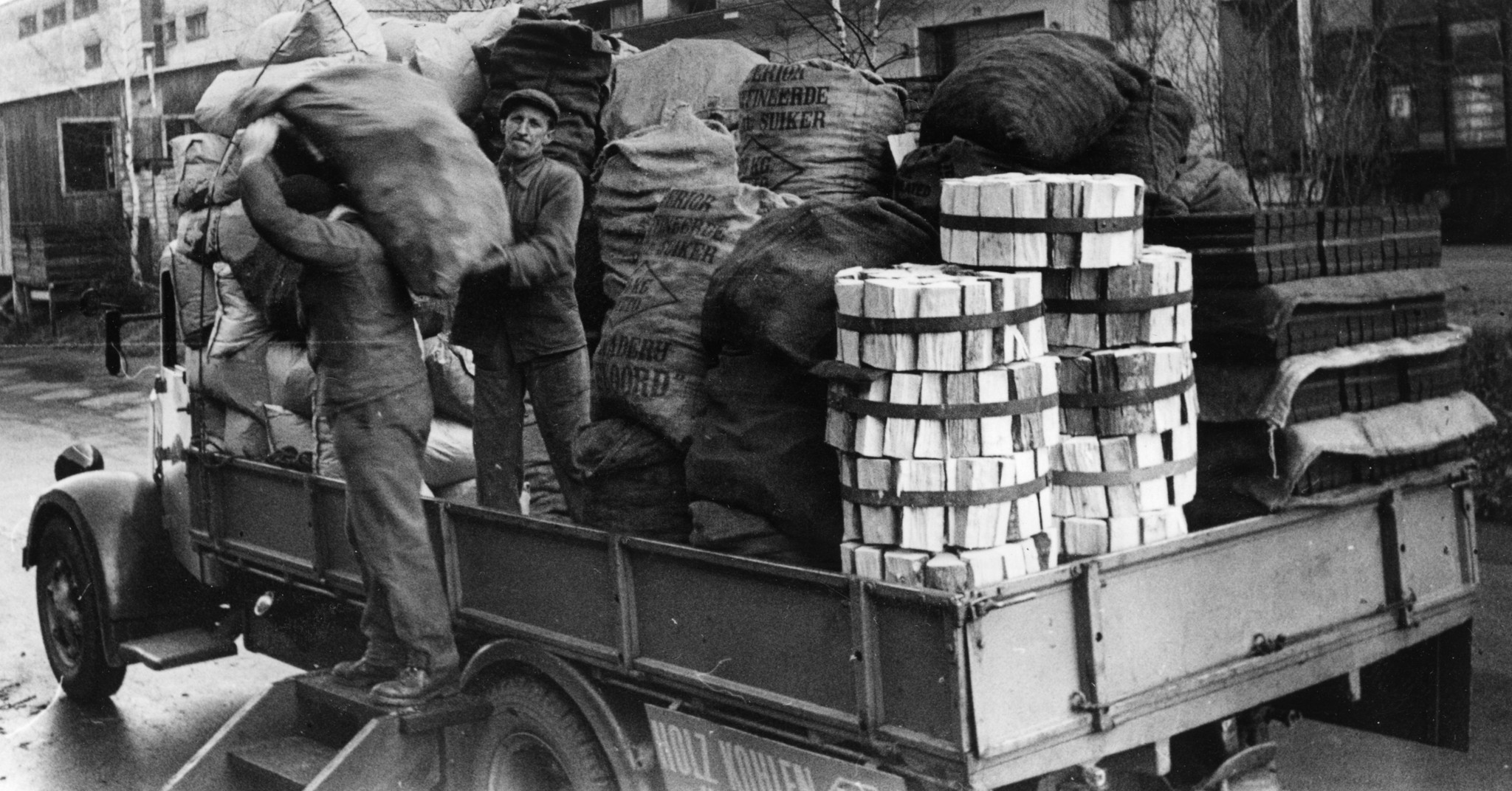 Kohle/Holz: Männer laden Holkohle und Holz von einem Lieferwagen ab