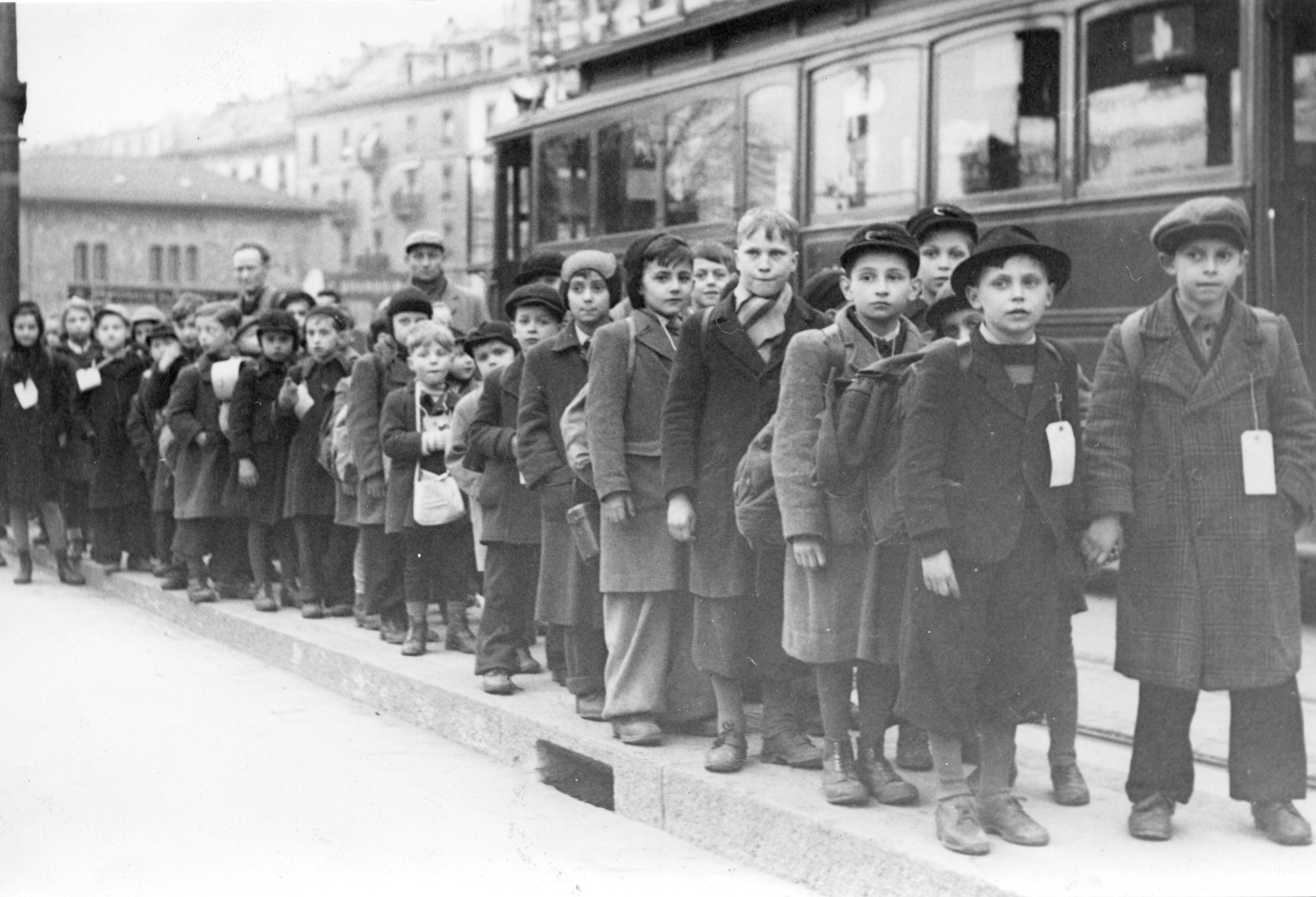 Kinder stehen in einer Reihe auf einem Bürgersteig, vermutlich auf einen Zug wartend
