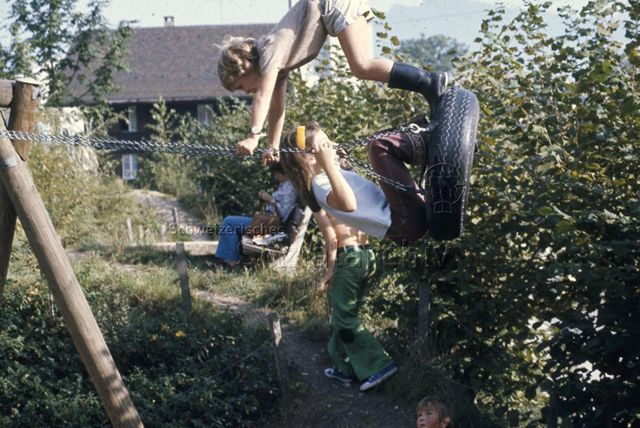 "Bauspielplatz St. Anton/Luzern" - Zwei Kinder auf einer Schaukel aus einem alten Reifeneins sitzend, eins stehend; 1975