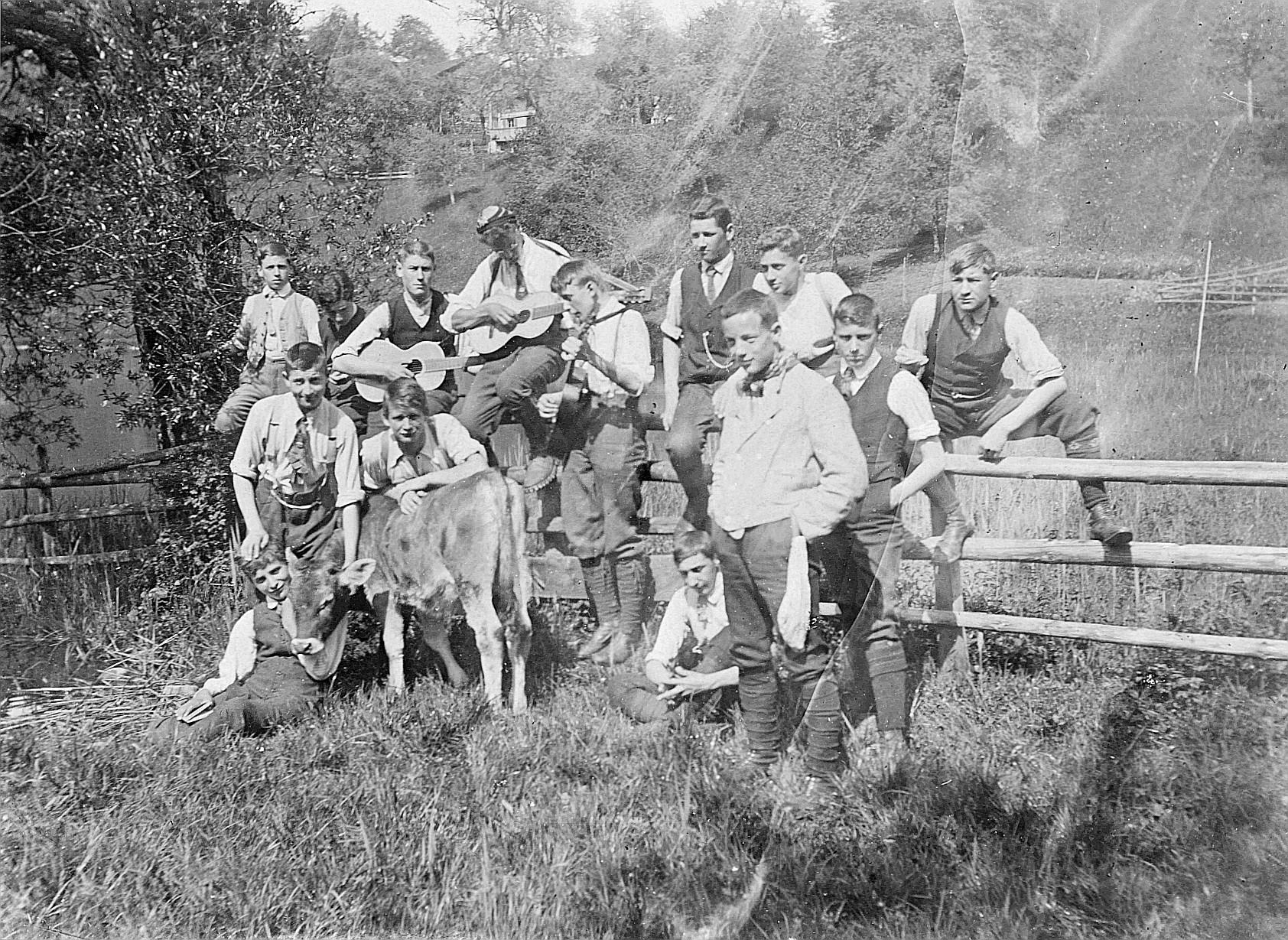 Gruppenporträt der Wandervögel, welche, zusammen mit einem Kalb, bei einem Bretterzaun posieren - Drei Wandervögel spielen Gitarre (