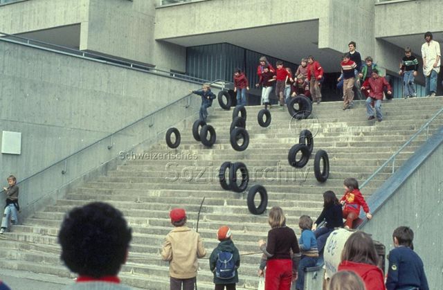 "Spielbus" - Kinder lassen alte Autoreifen über eine Treppe rollen; um 1975