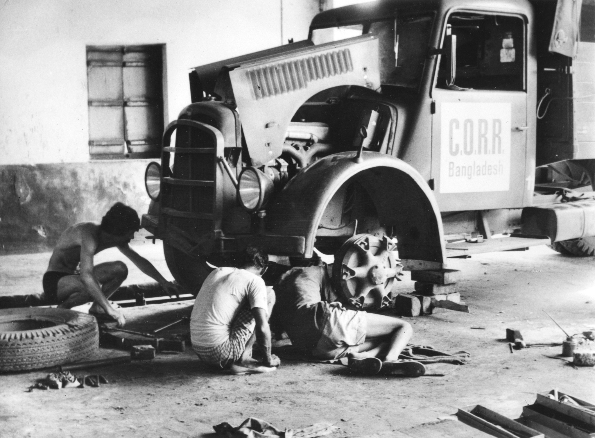 "Bangladesh: Swiss Truck Team Oktober 1972"; drei Männer warten einen Hilfsgüterlastwagen