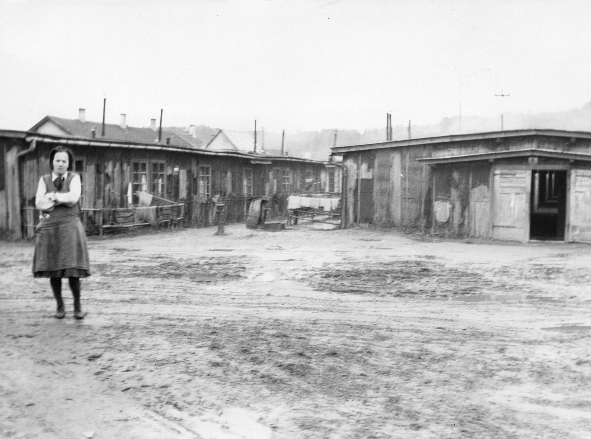 "Die Steyrerkinder wohnen in ehemaligen Gefangenenlagern. Auf der Ennsleitn in Steyer [Steyr in Oberösterreich]", Frau vor Wohnbaracken eines Lagers, um 1950 (Nachkriegszeit)
