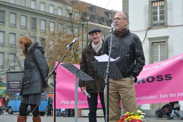 Kundgebung in Bern gegen die Familieninitiative der CVP (16.11.2013, Bern) – Rolf Trechsel am Mikrofon, hinten links: Alicia Parel, Banner des Pink Cross: "Keine Diskriminierung in unserer Verfassung, Finger weg! / Pas de discrimination dans notre constitution, bas les pattes! – Pink Cross"