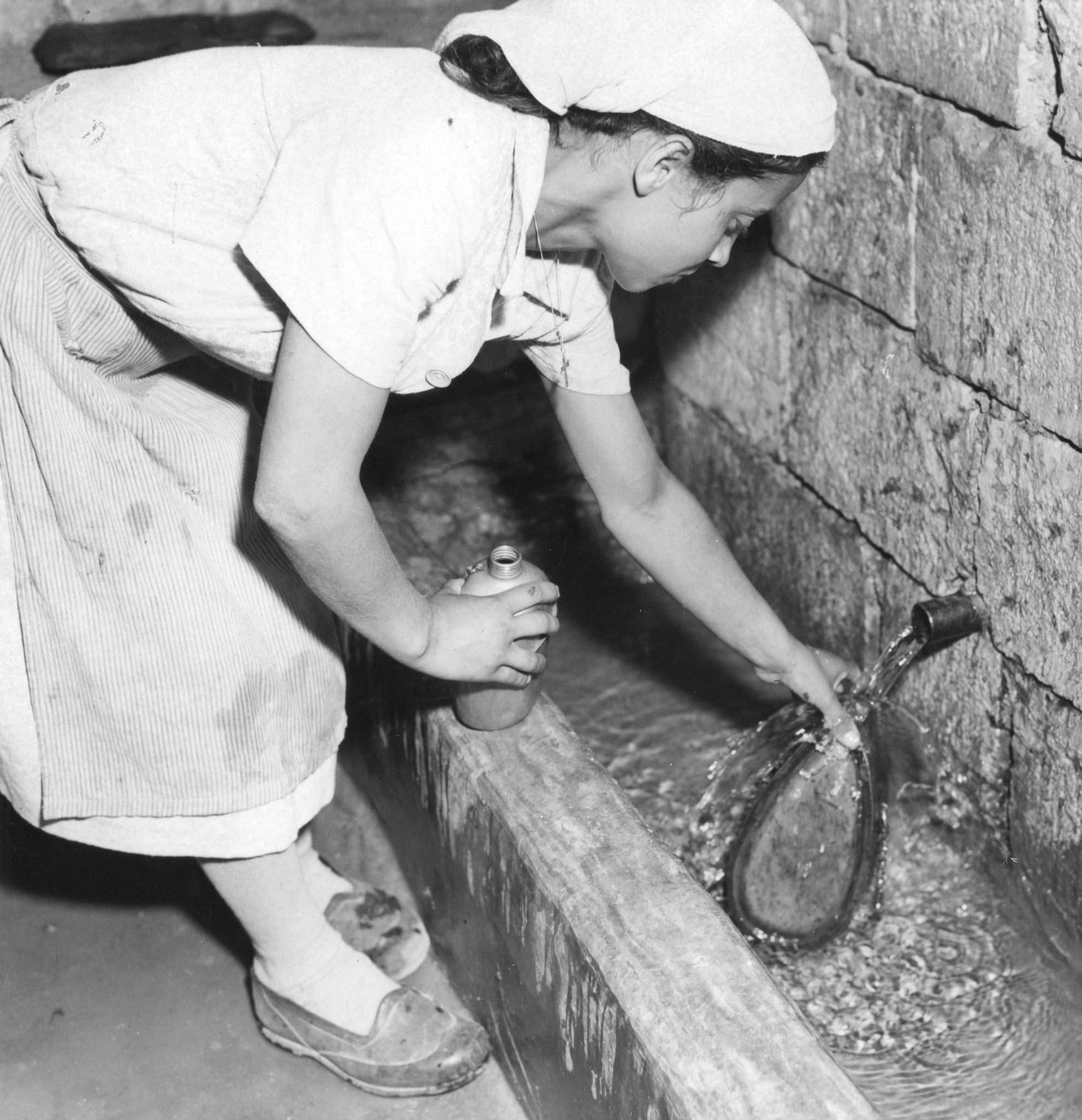 "New water supply in a Greek village. Aided by the Marshall Plan and their own efforts, the villagers built a new water supply by taping a spring a mile away and piping the water to the village. Greece". Wasserflaschen werden von einer Frau aufg