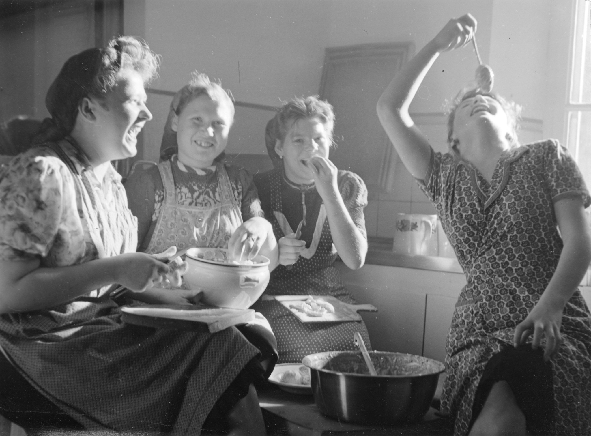 Vier Mädchen sitzen in der Küche und kochen, ein Mädchen probiert mit dem Löffel das Produkt
